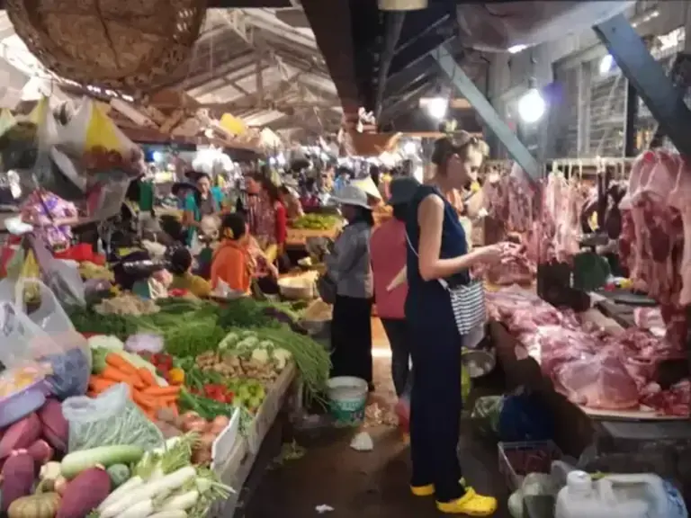 Narrow market aisle with vegetables on the left and meat on the right